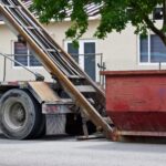 Roll-off truck unloading a dumpster at a job site